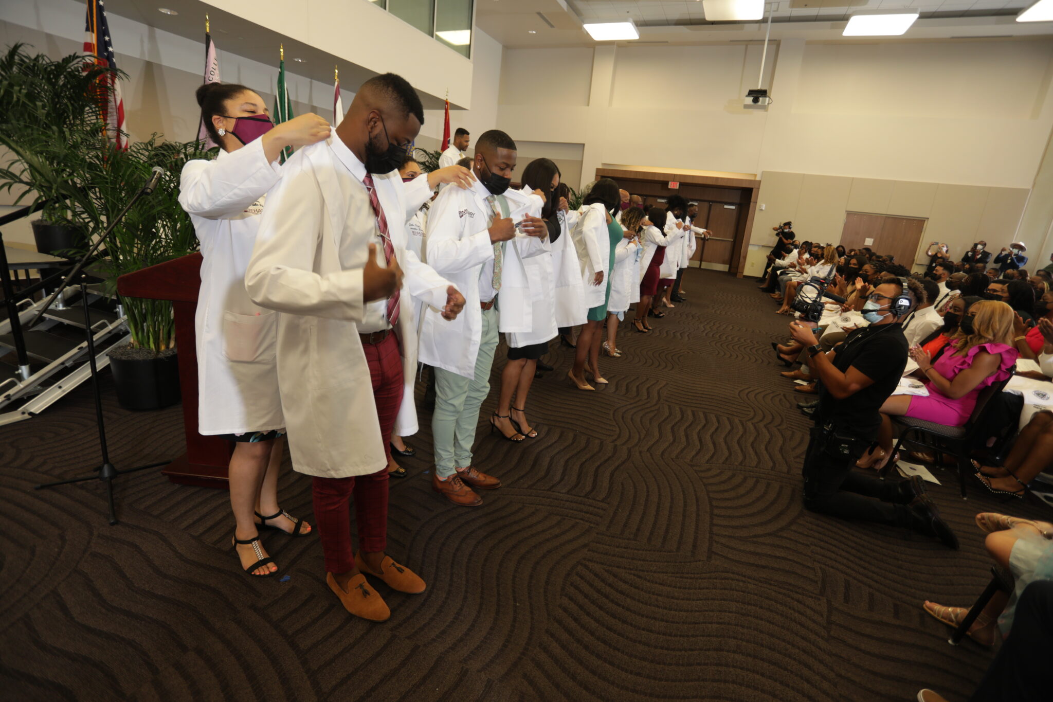 A group of people in lab coats, standing in a line, on a stage.