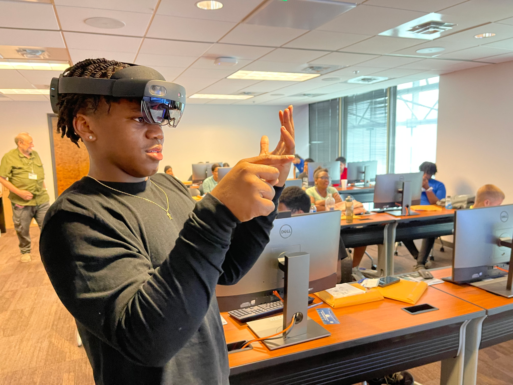 Man in black shirt holding camera in front of computer monitors.
