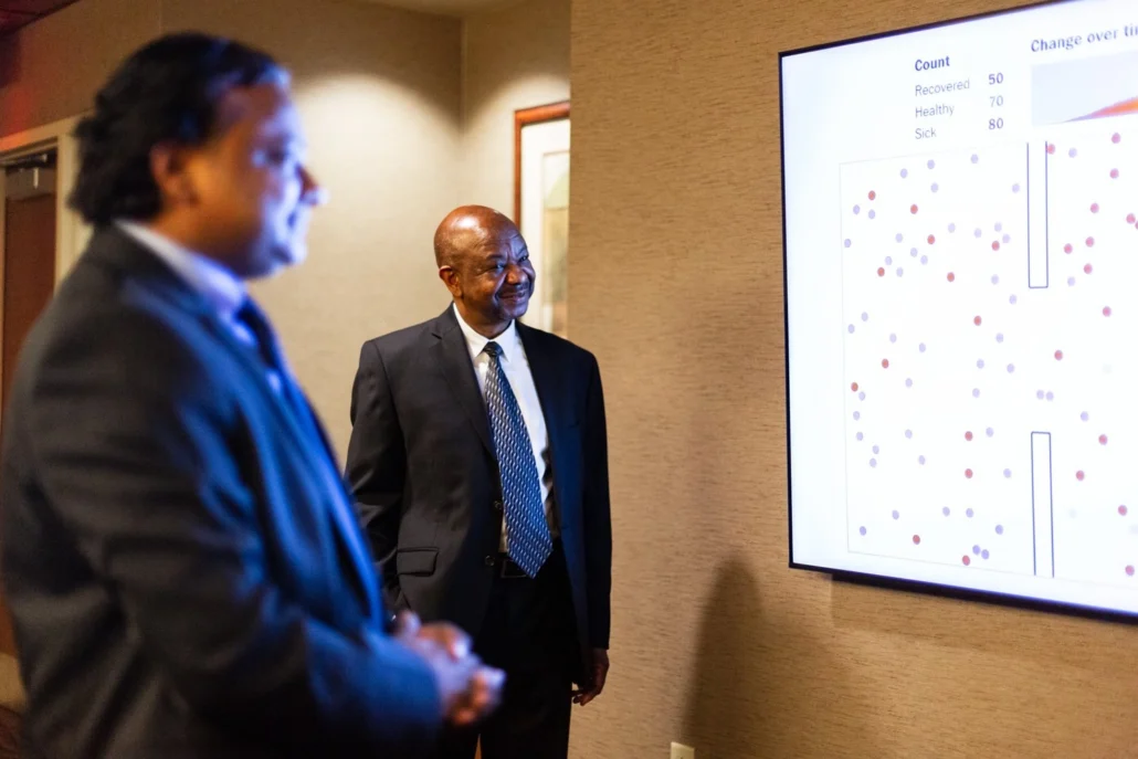 Two men standing in front of a large screen displaying a chart.
