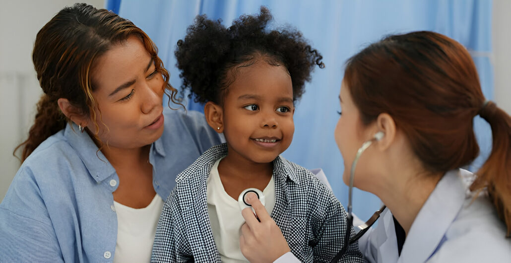 A family in a medical setting, with a woman holding a child and a doctor examining the child.