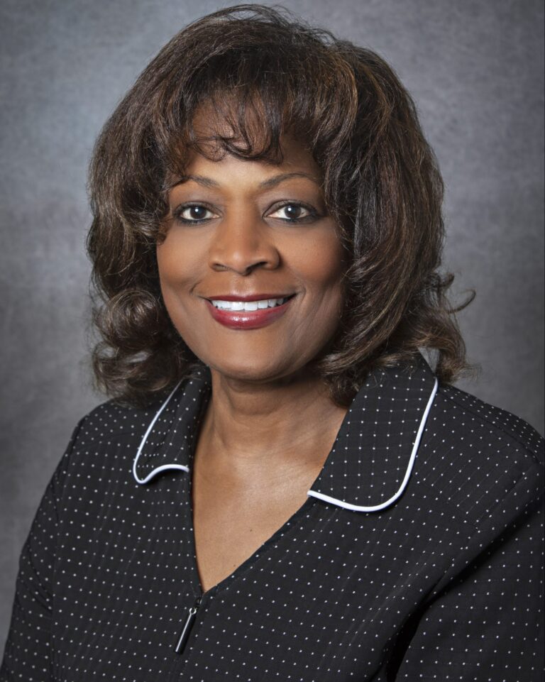 A woman in a black suit with a white shirt and polka dot tie, smiling and posing for a portrait.