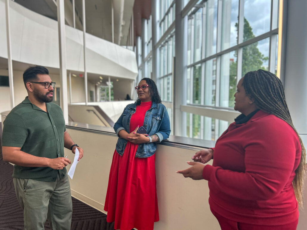 A man and woman standing in front of a large window, talking to each other.