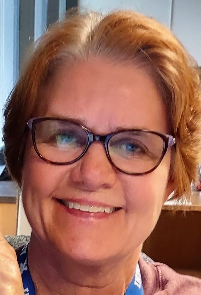 Woman wearing glasses, smiling, with short hair.