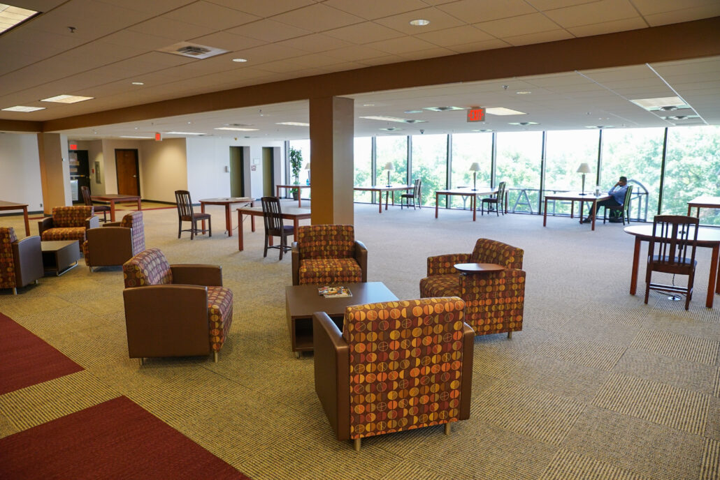 A spacious lobby with a variety of seating options, including chairs and couches, arranged around a large table.