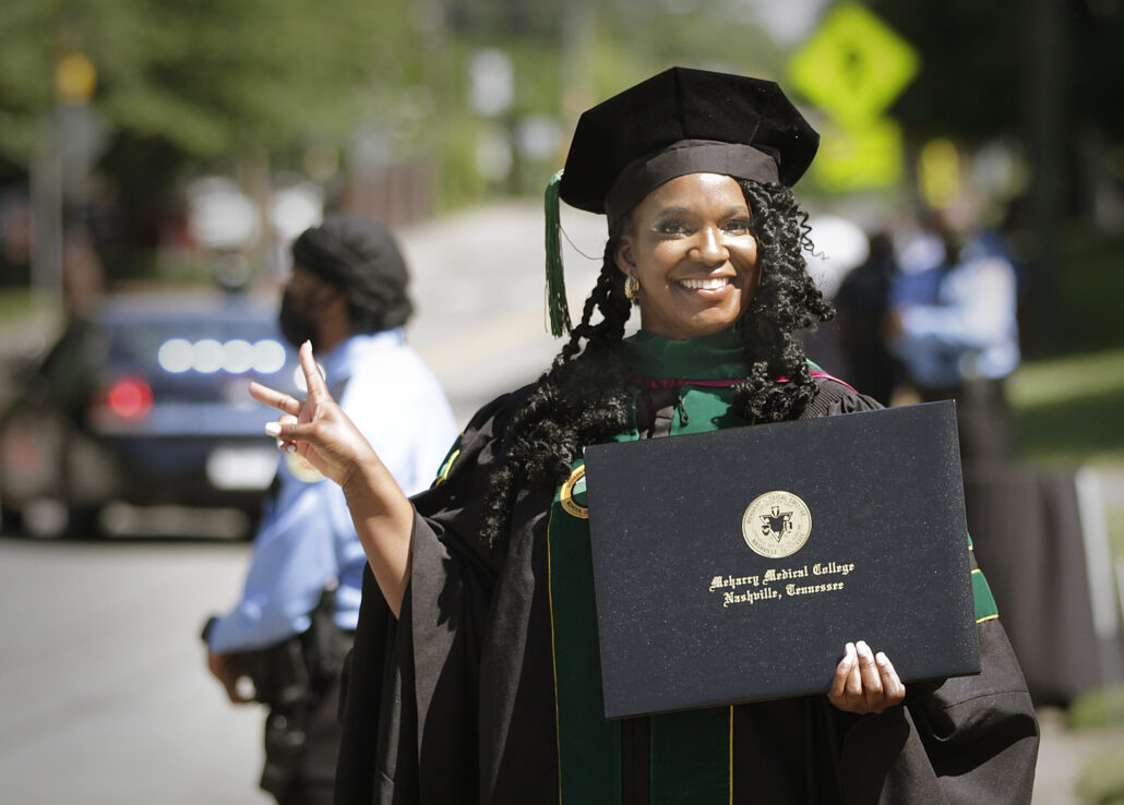 Woman in graduation cap and gown holding diploma, smiling and giving peace sign.