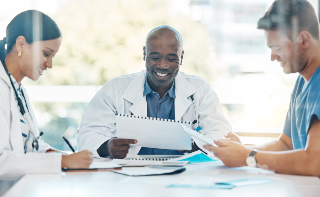 A group of people, including a doctor, gathered around a table with papers, smiling and looking at the camera.