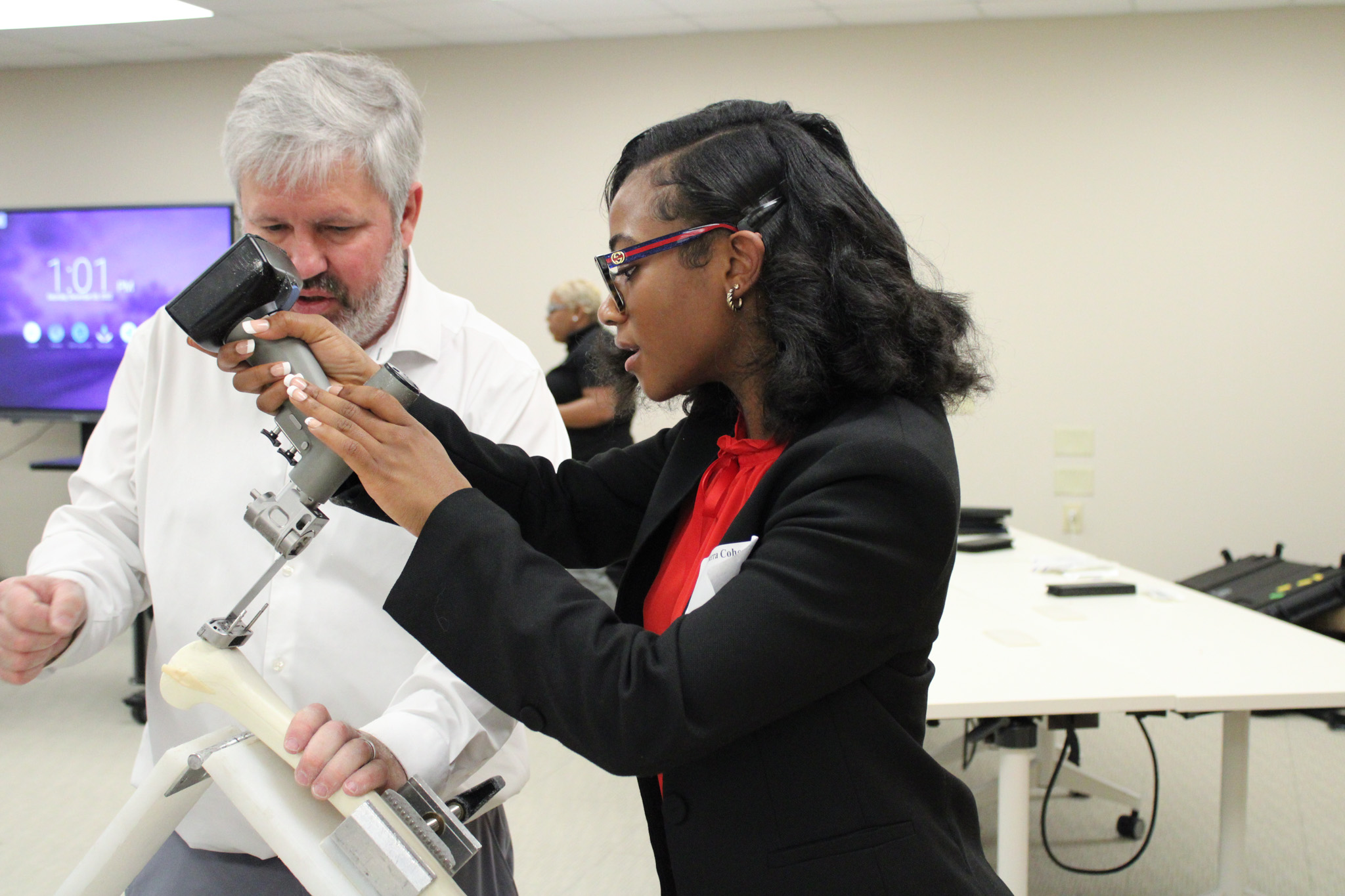 Two people examining a microscope, one woman holding a microscope, another man observing.