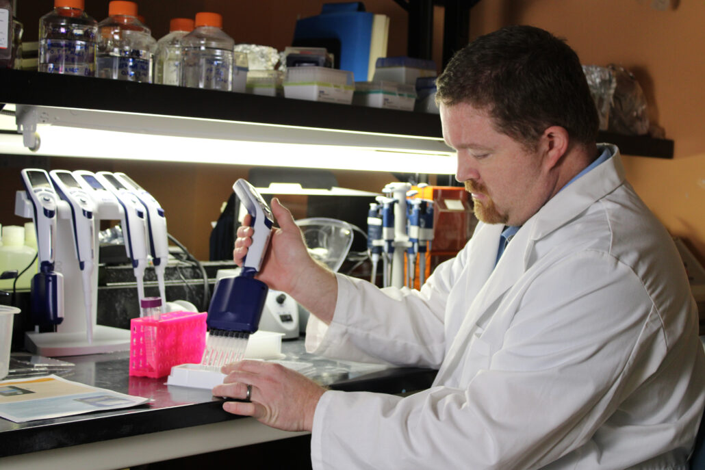Man in lab coat examining microscope.