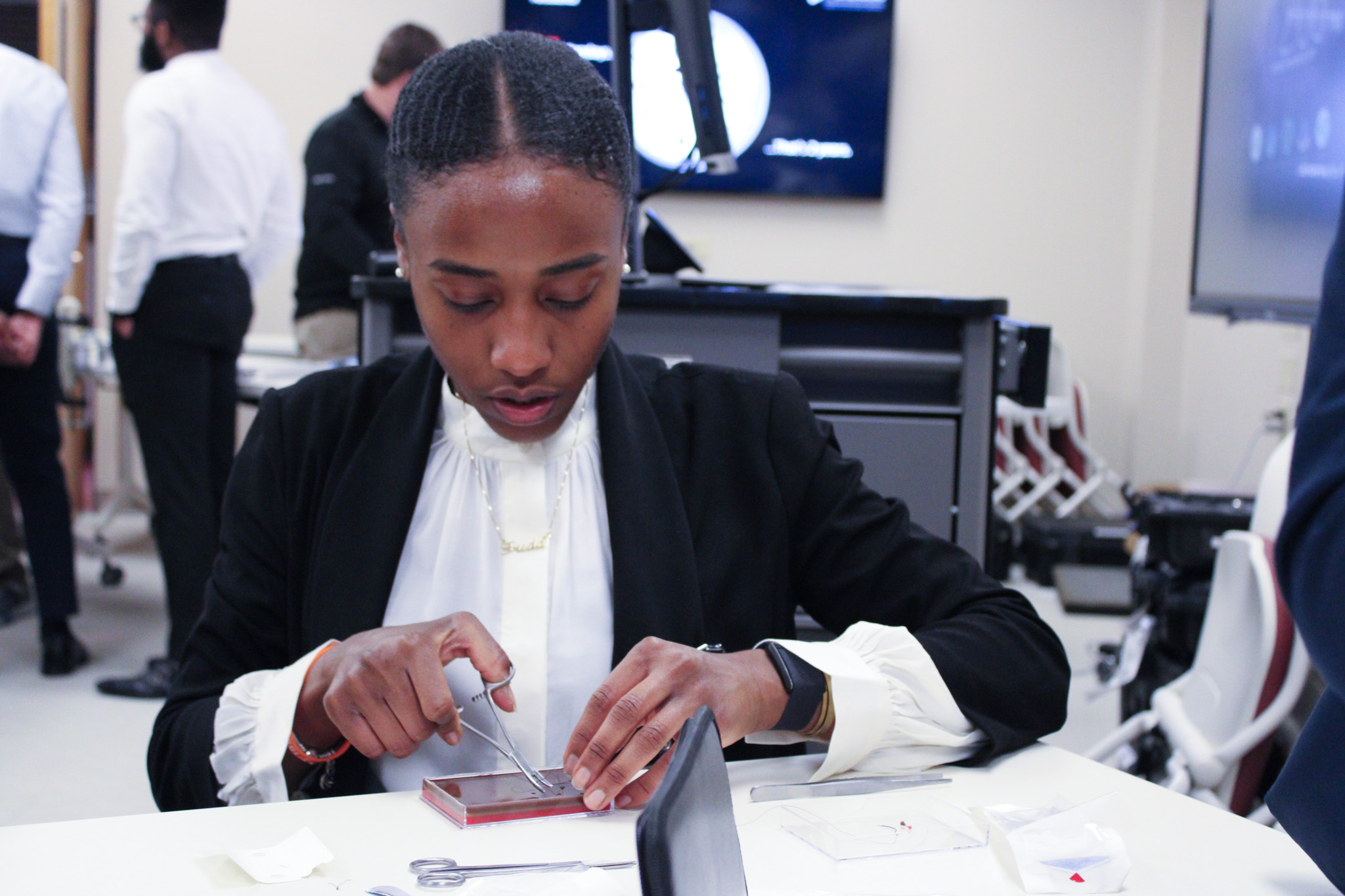 Woman in black suit sitting at desk, working on laptop.