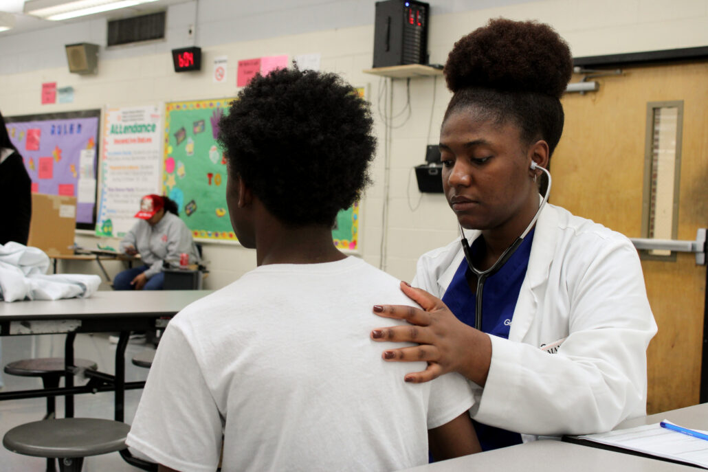 Woman in white coat, stethoscope around neck, standing behind boy.