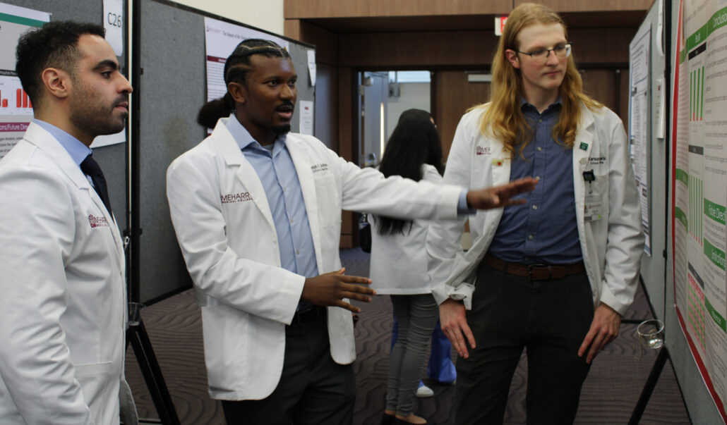 A group of people, including doctors, standing around a display board with posters.