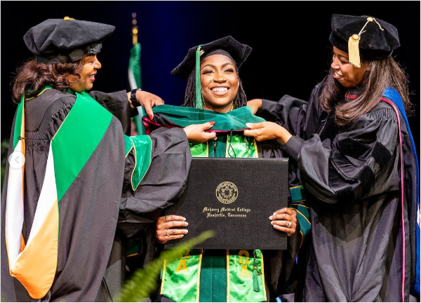 Two women in graduation gowns pinning a medal on a graduate.
