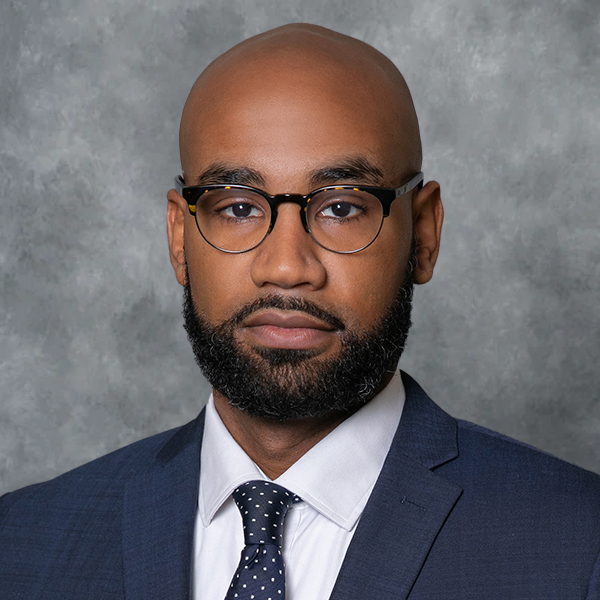 Man in suit and glasses, bald head, beard, looking directly at camera.