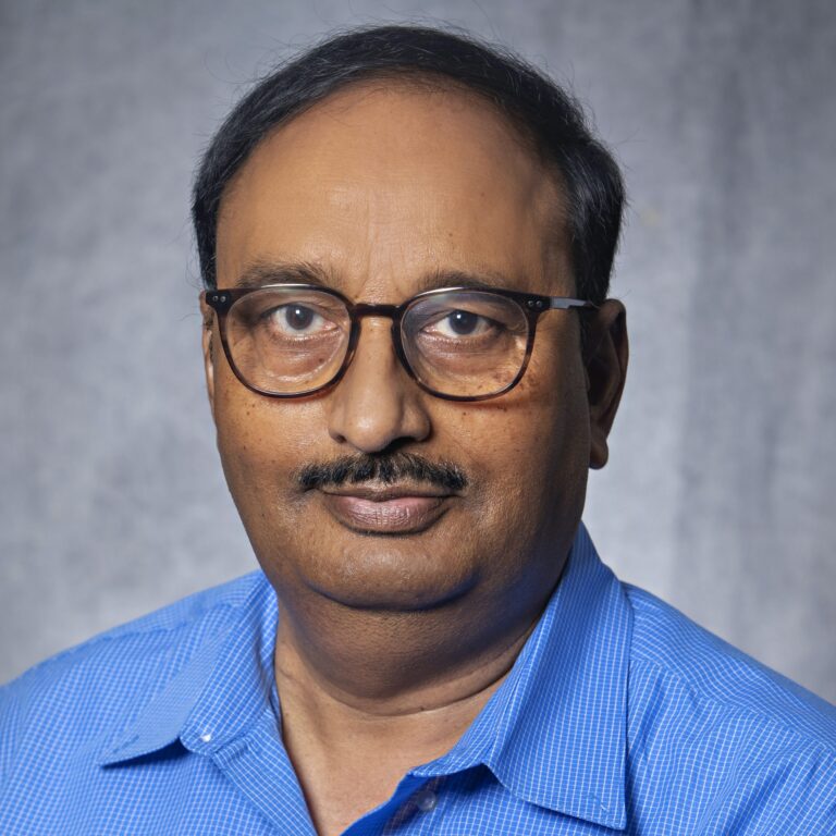 Man in glasses, blue shirt, smiling, posing for portrait.
