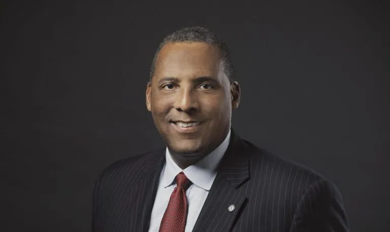 A man in suit standing against a dark background.