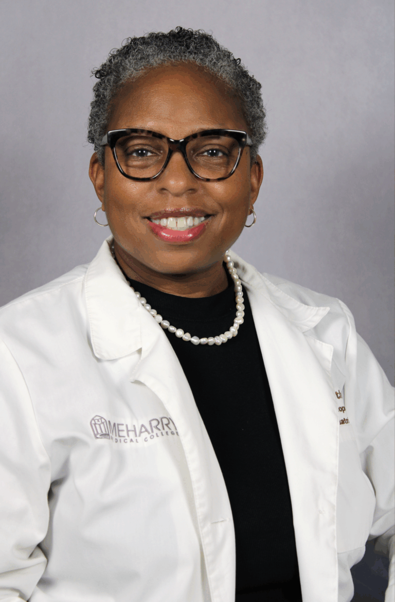 Woman in white coat, smiling, posing for photo.