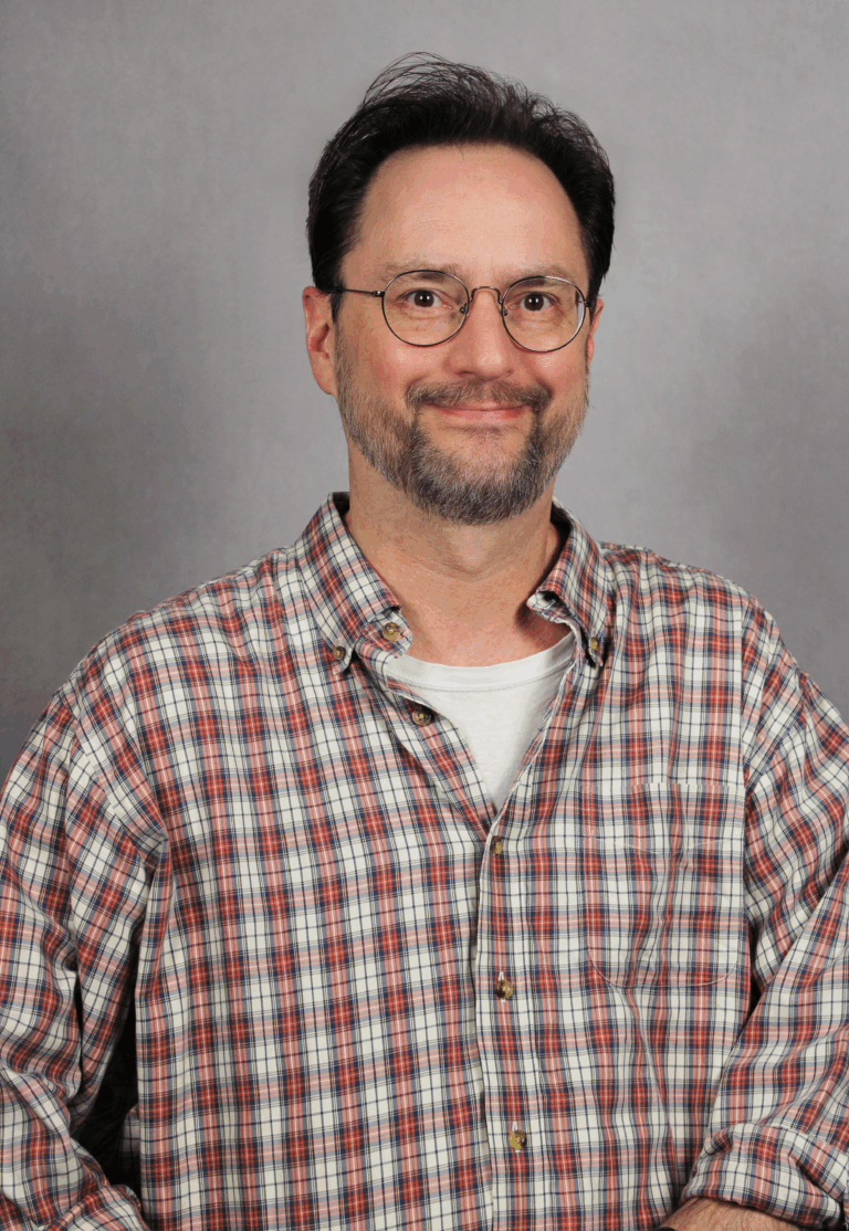 Man in plaid shirt smiling at camera.