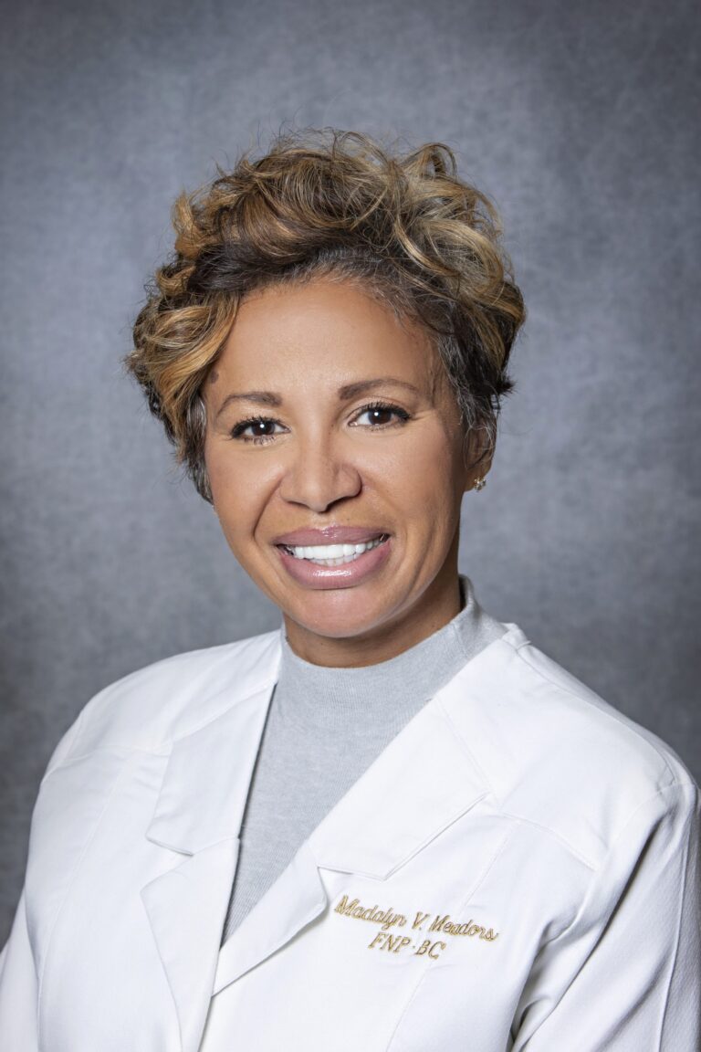Woman in white coat smiling, posing for photo.
