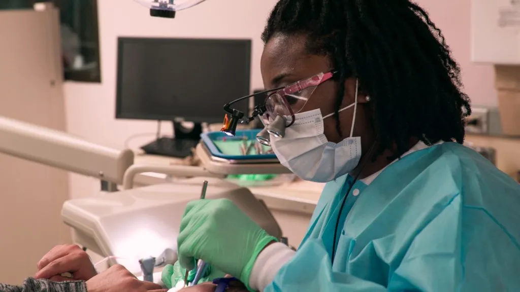Woman in a mask and scrubs working at a dental station.