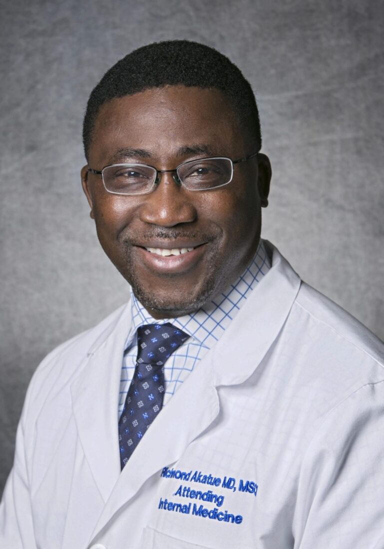 Man in lab coat smiling, glasses, balding, smiling.
