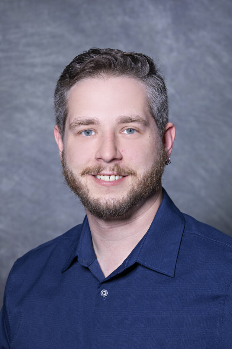 Man in blue shirt smiling at camera.