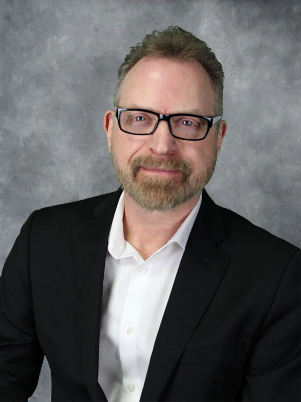Man in suit, glasses, beard, smiling.