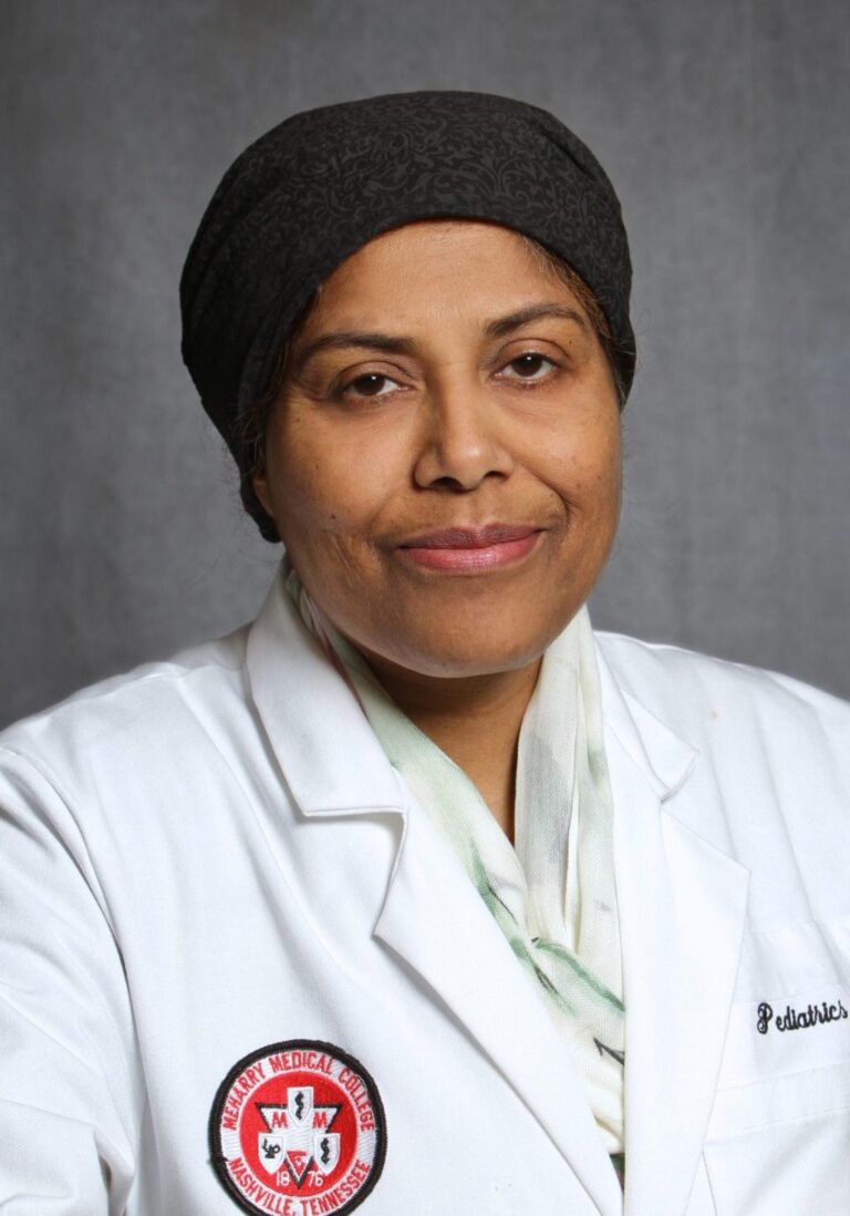 Woman in white coat, black headscarf, smiling at camera.