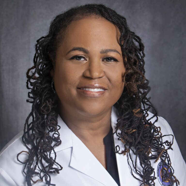 Woman in white coat, smiling, posing for photo.