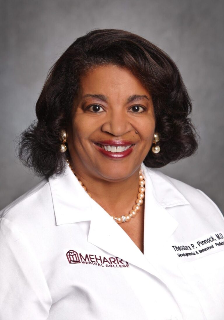 Woman in white coat smiling, posing for portrait.
