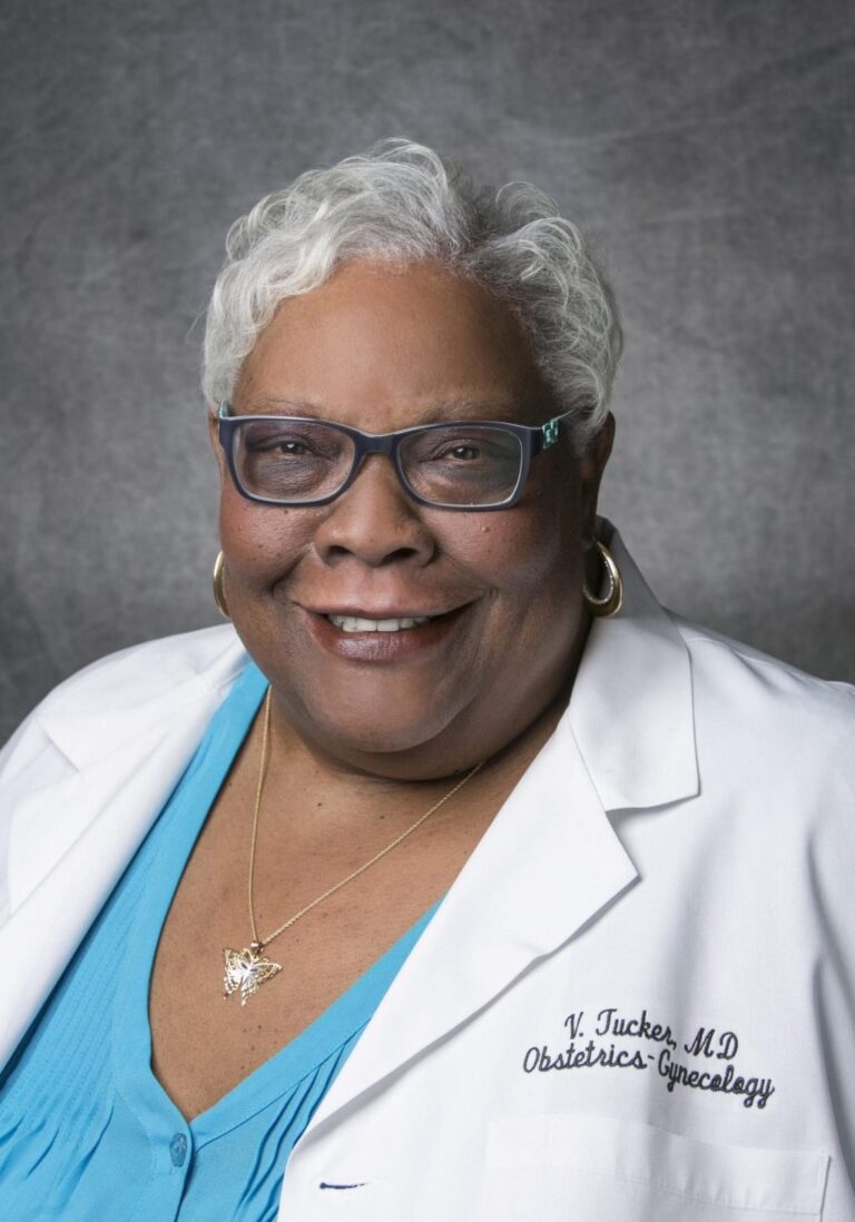 Older woman in white coat, smiling, posing for portrait.