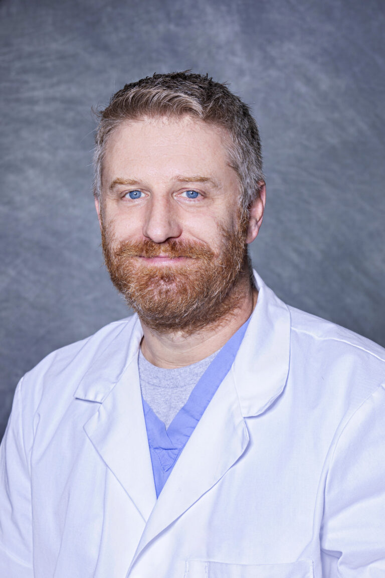 Man in white coat, smiling, posing for portrait.