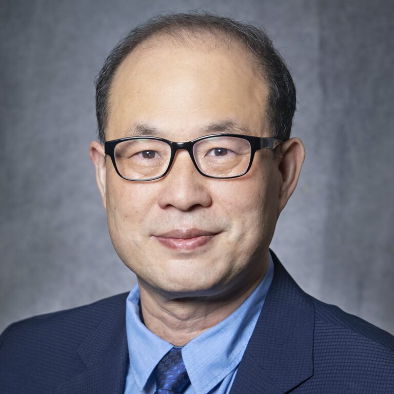 Man in glasses, suit, and blue shirt posing for portrait.