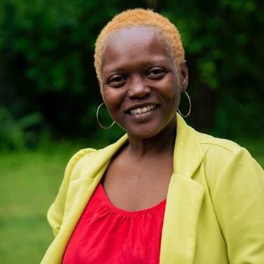 A woman with short hair, wearing a yellow top and a red dress, smiling at the camera.
