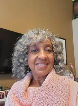 Woman with curly hair, smiling, wearing a pink scarf and a blue sweater.