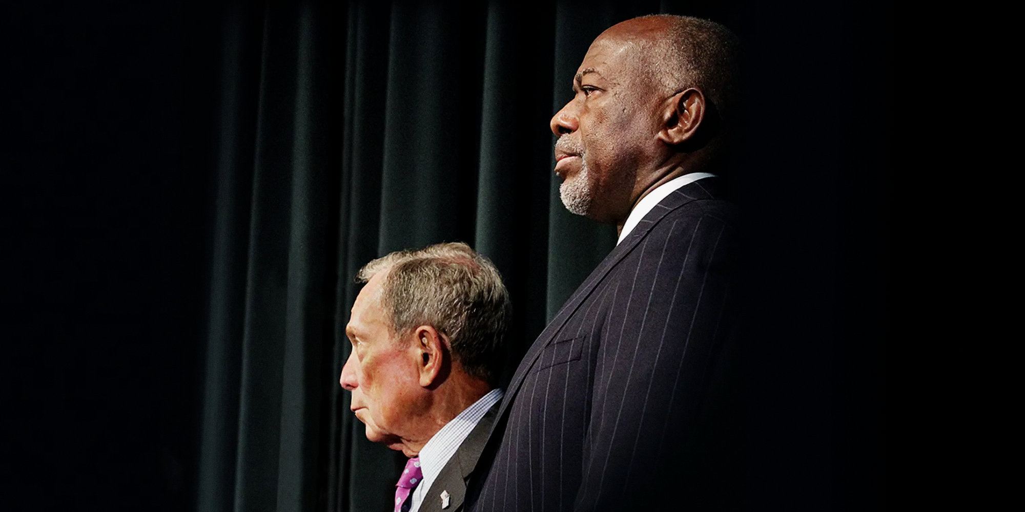 Two men standing side by side, one with a tie, in front of a podium.
