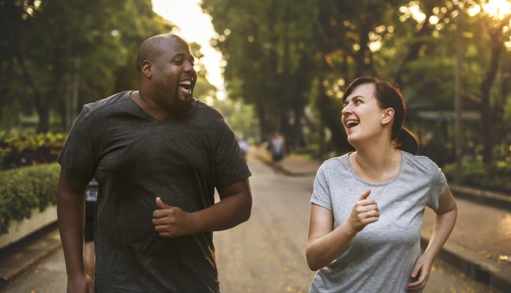 Two people jogging on street. Man in front, woman behind. Both smiling, man in black shirt, woman in white shirt.