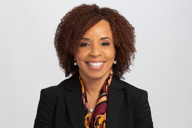 Woman with curly hair, smiling, wearing a black jacket and a patterned scarf.