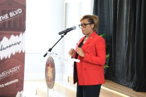 Woman in red jacket speaking at podium.