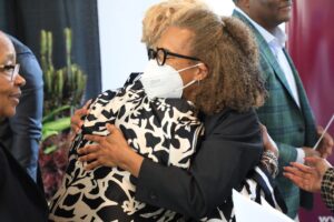 Two women hugging, one wearing a mask.