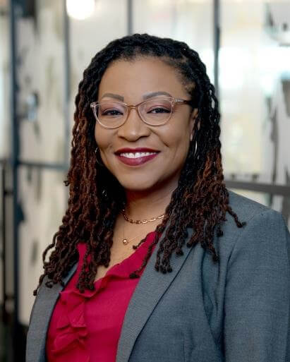 A woman in a suit stands confidently, smiling at the camera.