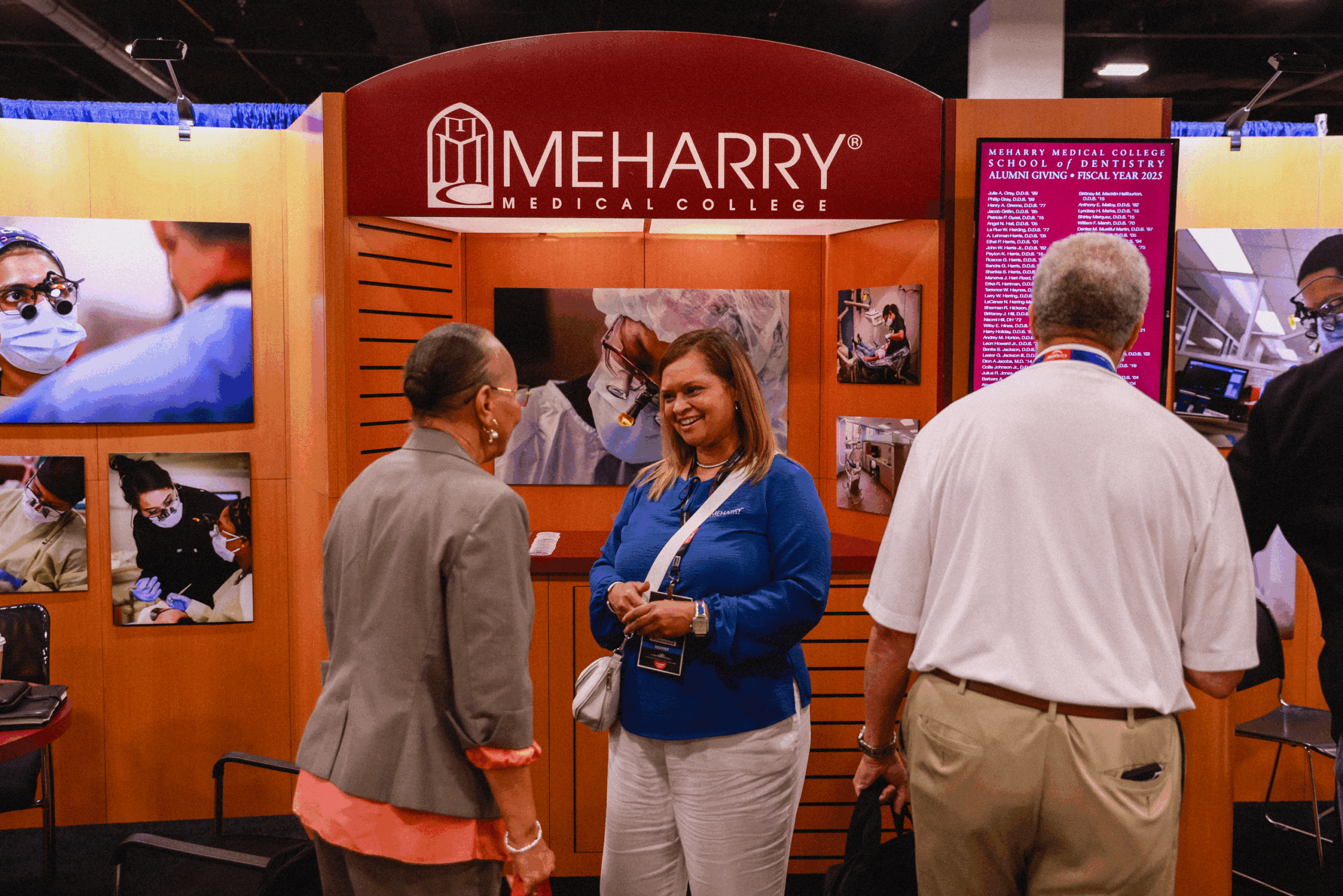 People standing in front of a booth with a large screen displaying photos. The booth has a sign that says "Mhearry".