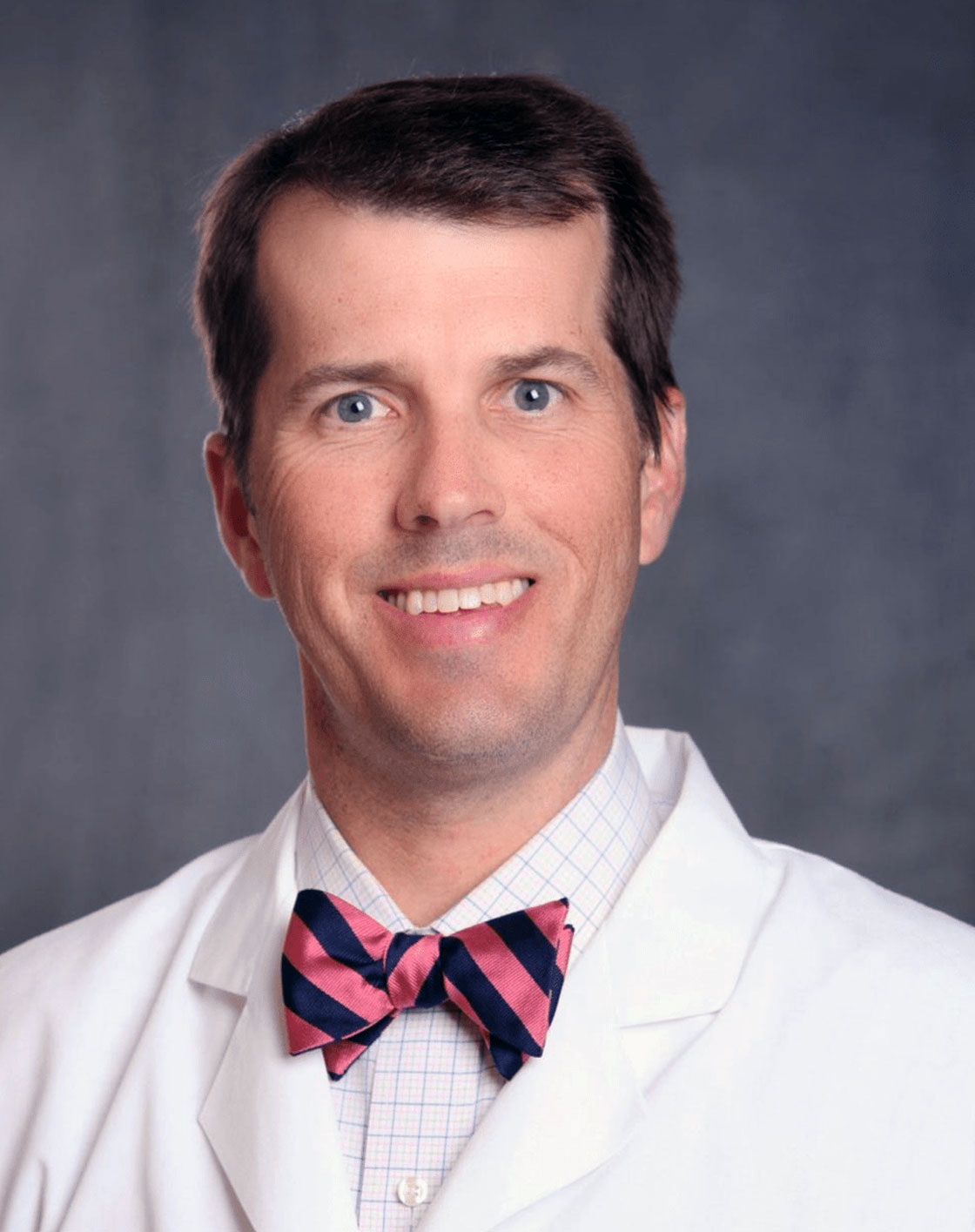 Man in white coat and bow tie, smiling.