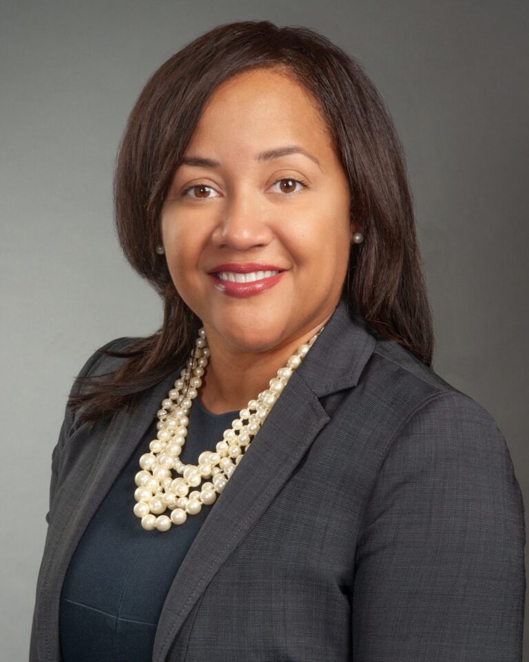 A woman in a suit, smiling, posing for a portrait.