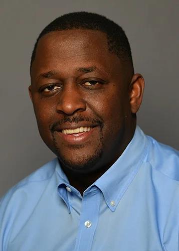 A man in a blue shirt smiling at the camera.