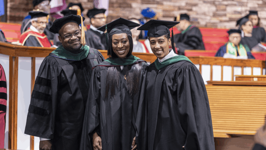 Three graduates posing on stage.