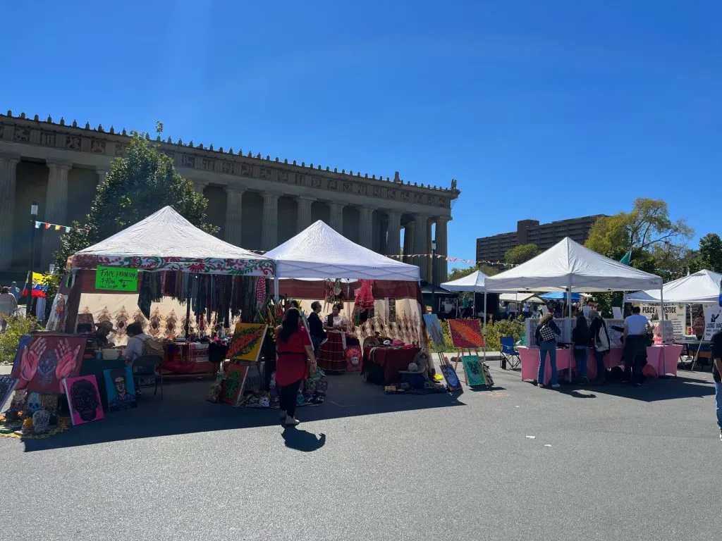 Outdoor market with several vendor tents, people browsing, and a clear sky.