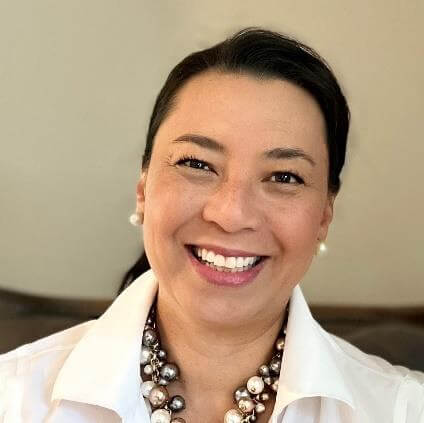 A woman with a radiant smile, wearing a white top and pearls.