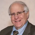 Old man with glasses, smiling, wearing a suit.