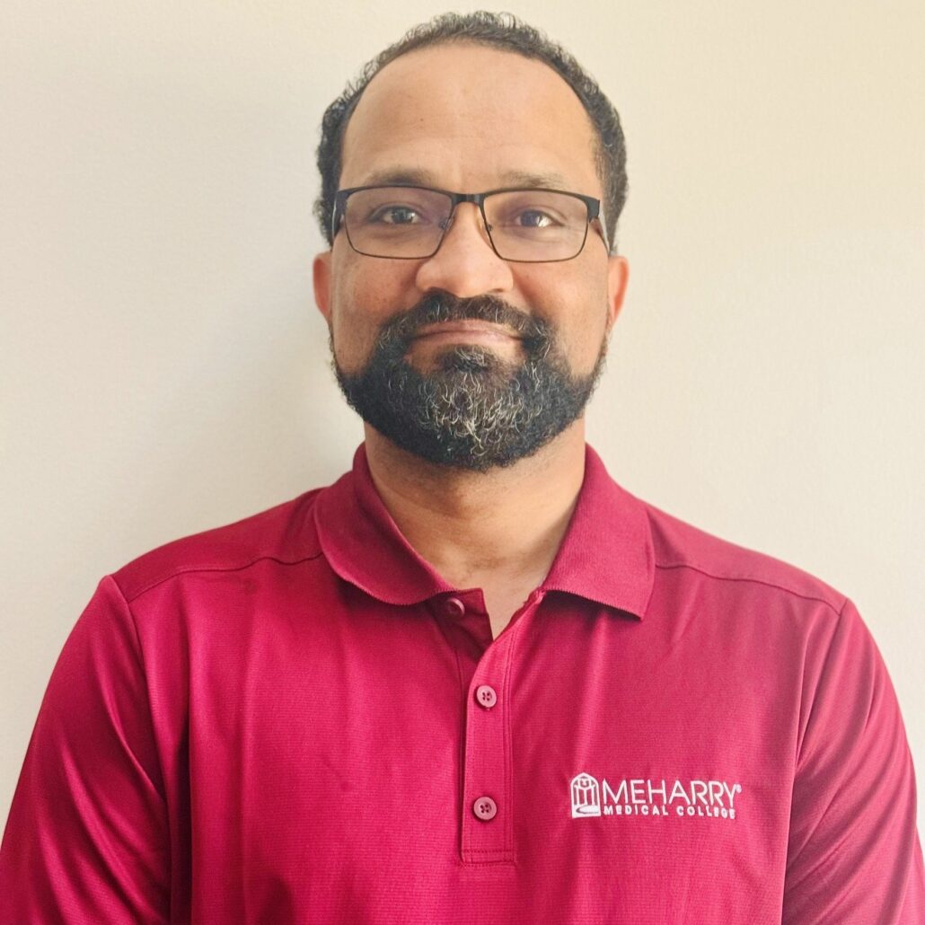 Man in red shirt and glasses, smiling at camera.