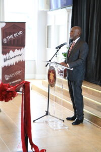 Man standing at podium in front of red rope barrier.